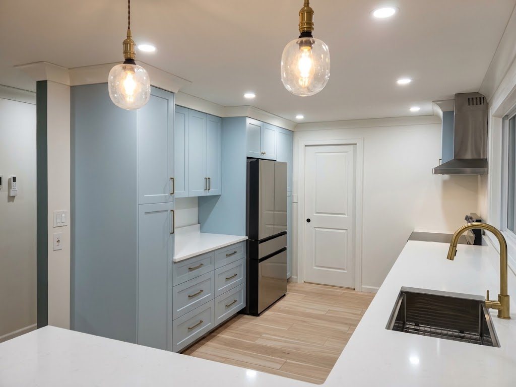 Renovated kitchen in West Sechelt with pale blue shaker cabinets and a pantry wall, white quartz counters, an undermount sink with a brass faucet, glass pendant lights and a white door at the back