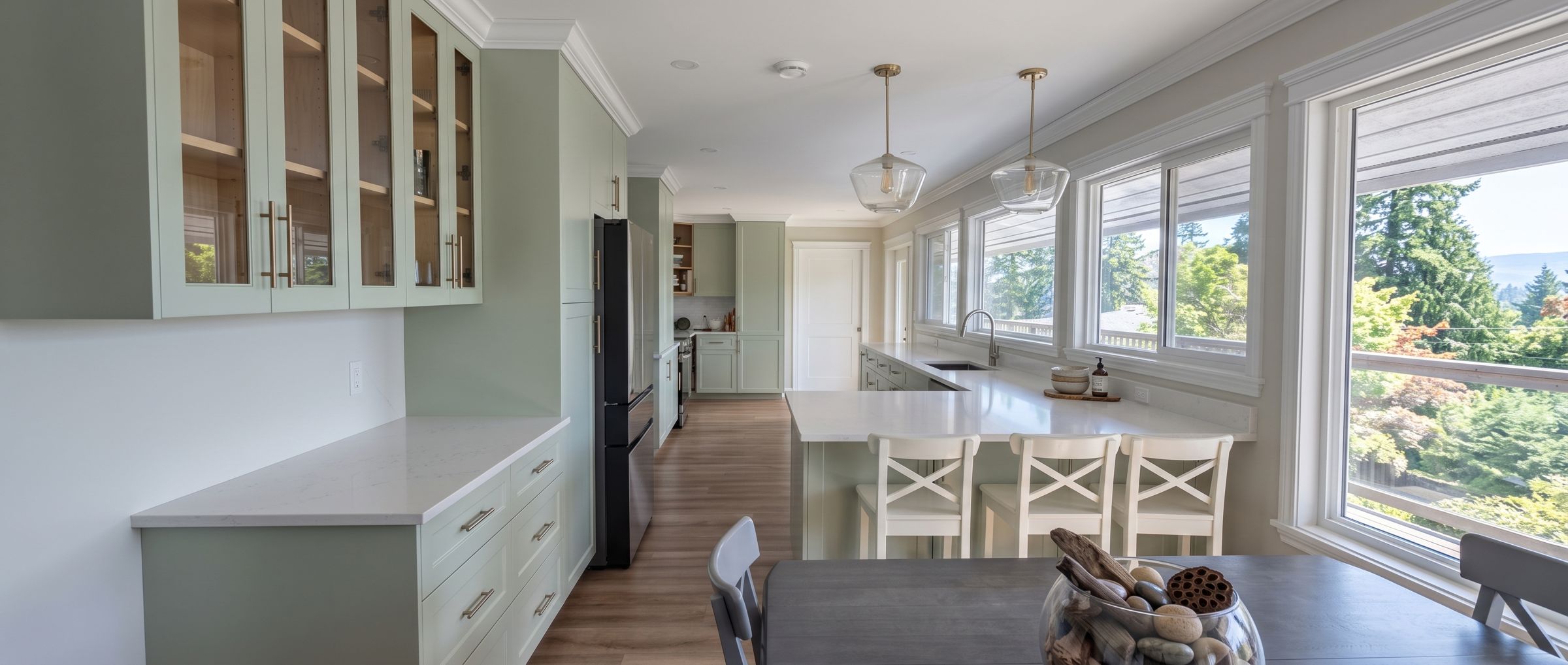 Renovated kitchen in West Sechelt with sage-green shaker cabinets, white quartz counters and a long peninsula under a row of windows