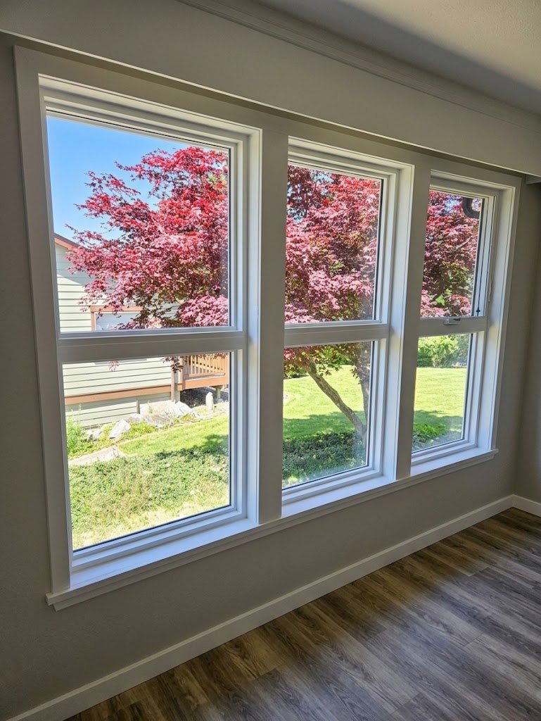 Three new white windows in a West Sechelt home, finished with wide white trim inside, looking out on a red Japanese maple