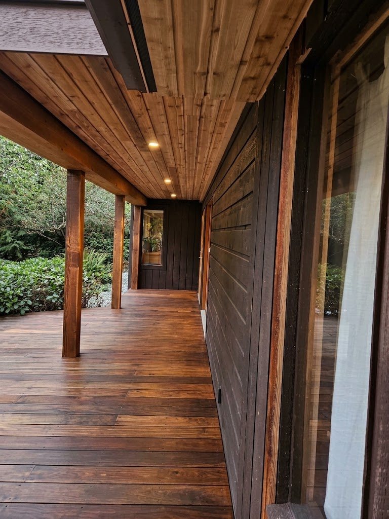 Covered porch under the upper deck, with cedar ceiling, LED pot lights, timber posts and a wood deck along the dark cedar siding