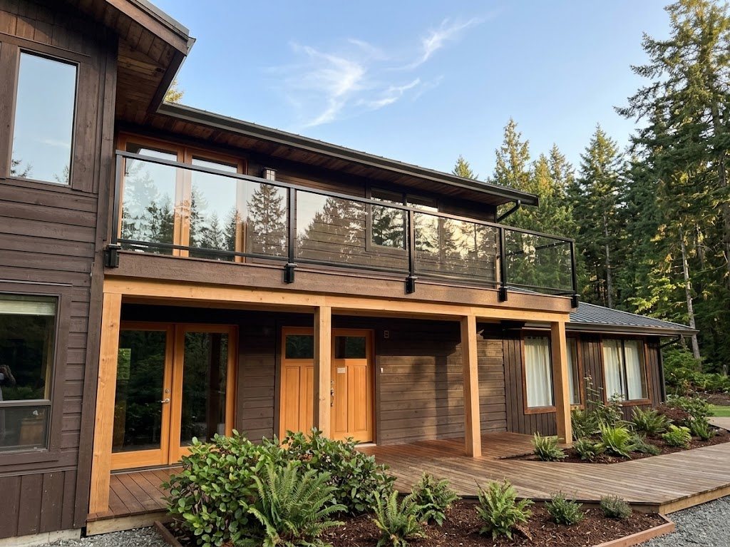 Two-storey Wilson Creek home with a new Trex upper deck and glass guardrails over a covered porch with timber posts, cedar soffit and a wood entry deck